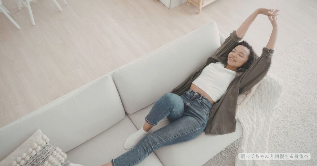 ソファでくつろぎながら、両腕を上げて気持ちよく背伸びをする女性