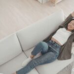ソファでくつろぎながら、両腕を上げて気持ちよく背伸びをする女性